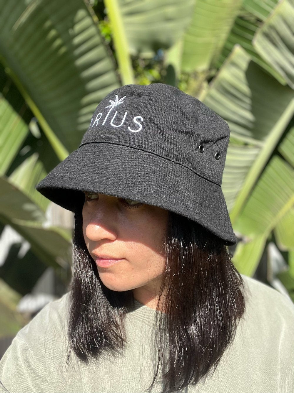 Black bucket hat made from recycled cotton and recycled polyester. Features a white embroidered logo. Available in sizes S/M and M/L. Ethically produced with certifications and shipped in eco-friendly packaging.